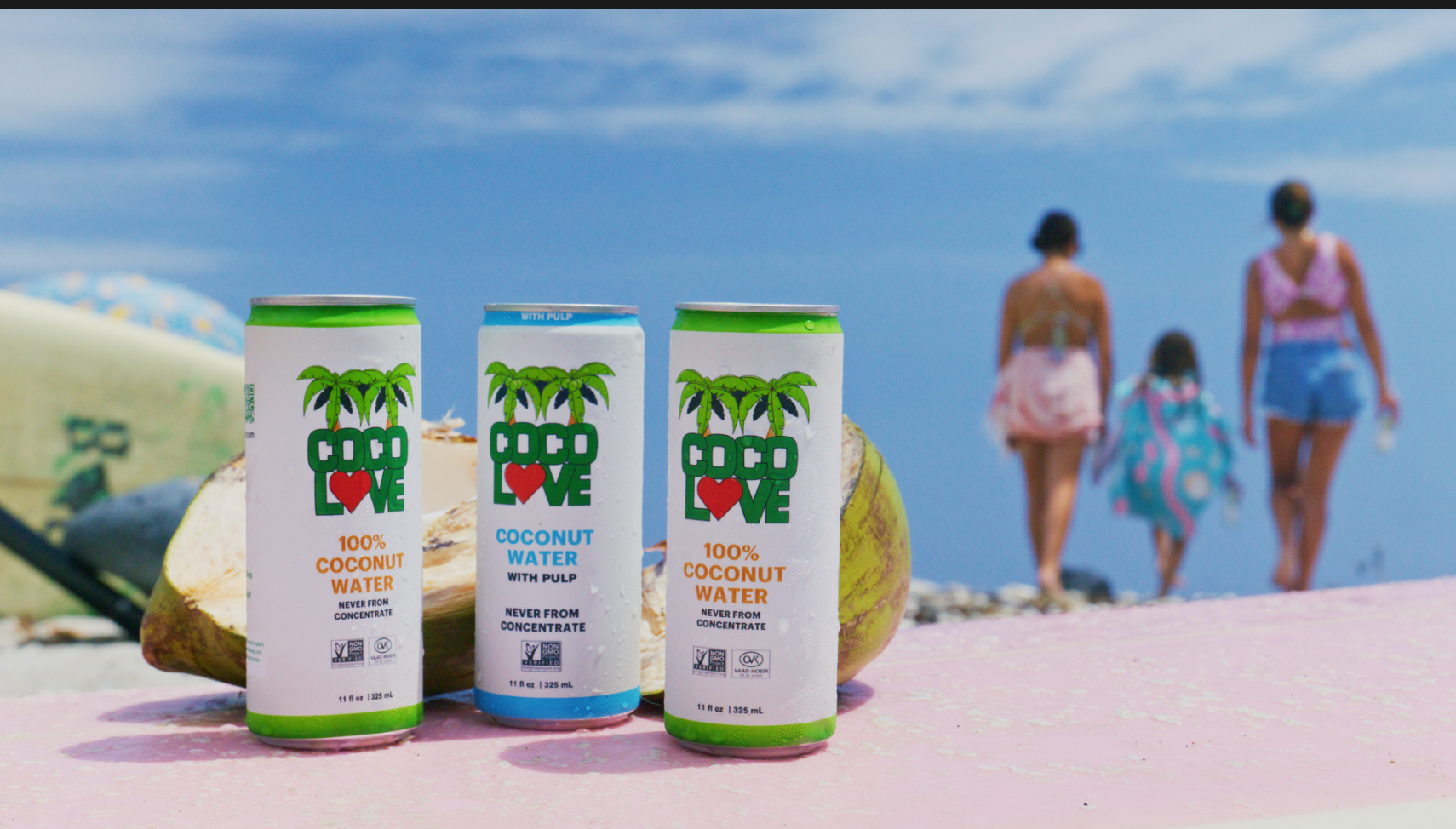 CocoLove coconut water cans on the beach with a family in the background